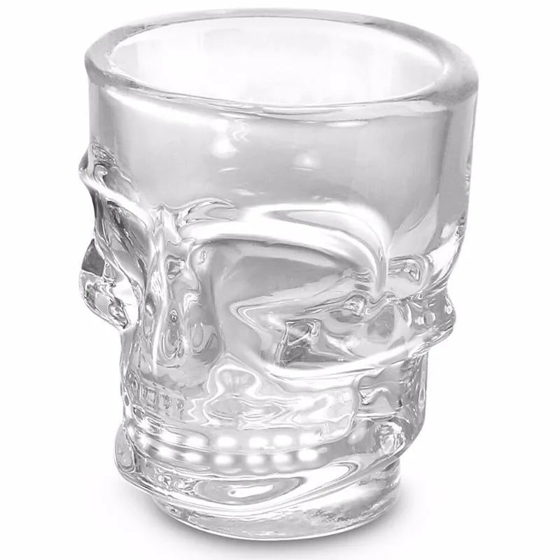 Verre à shooter transparent en forme de crâne, vide, montrant le relief sculpté du visage sur fond blanc.
