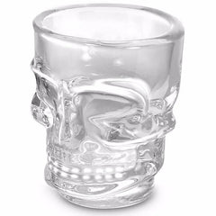 Verre à shooter transparent en forme de crâne, vide, montrant le relief sculpté du visage sur fond blanc.