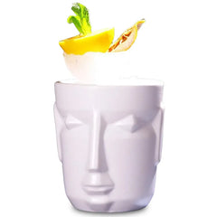 Packshot sur fond blanc du verre à cocktail tiki blanc en forme de visage, garni d'un quartier de citron, d'un fruit séché et de menthe fraîche