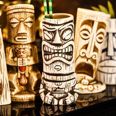 Verre à cocktail Tiki Maori présenté au milieu d'une collection d'autres mugs tiki sur une étagère de bar