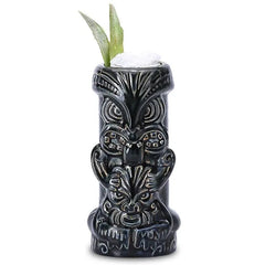 Verre à cocktail Tiki Dieu Noir rempli de glace pilée avec une garniture végétale sur fond blanc