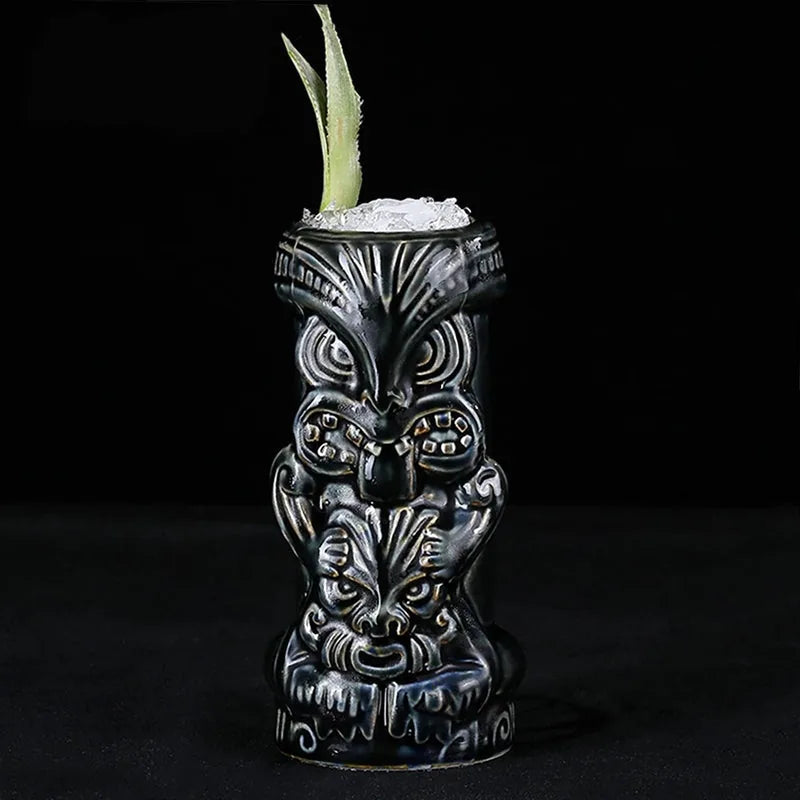 Verre à cocktail Tiki Dieu Noir rempli de glace pilée et garni d'une feuille verte, photographié sur fond noir