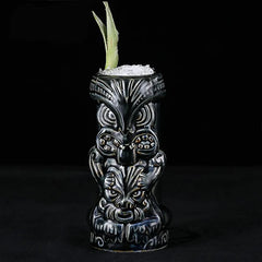 Verre à cocktail Tiki Dieu Noir rempli de glace pilée et garni d'une feuille verte, photographié sur fond noir