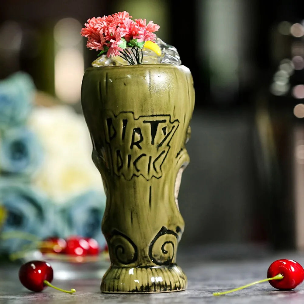 Le verre tiki vert avec l'inscription gravée « Dirty Dick », garni de fleurs roses et de glaçons, entouré de cerises.