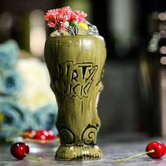 Le verre tiki vert avec l'inscription gravée « Dirty Dick », garni de fleurs roses et de glaçons, entouré de cerises.