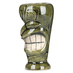 Verre à cocktail tiki vert au visage grimaçant, photographié de profil sur fond blanc.