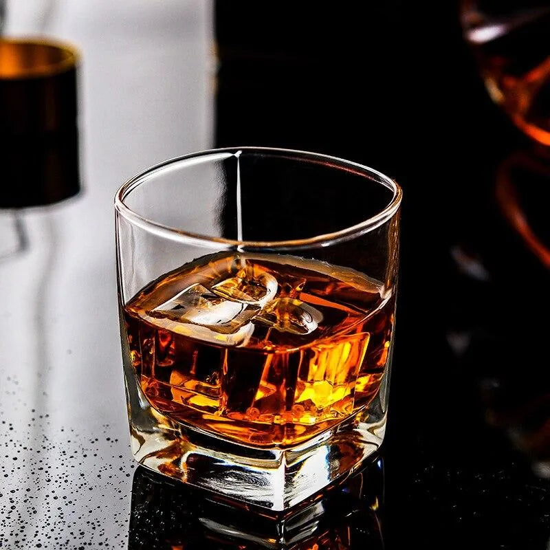 Verre à whisky fond épais avec glaçons et whisky, posé sur une surface sombre réfléchissante