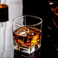 Verre à whisky fond épais avec glaçons et whisky, posé sur une surface sombre réfléchissante