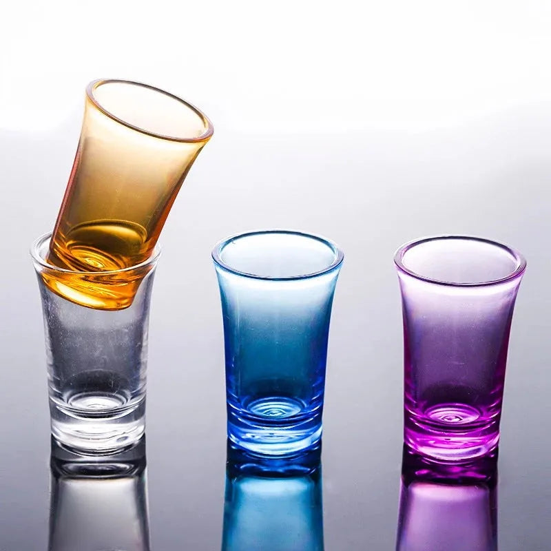 Verre à shot orange incliné en train d'être versé dans un verre transparent, à côté des versions bleue et violette.