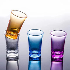 Verre à shot orange incliné en train d'être versé dans un verre transparent, à côté des versions bleue et violette.