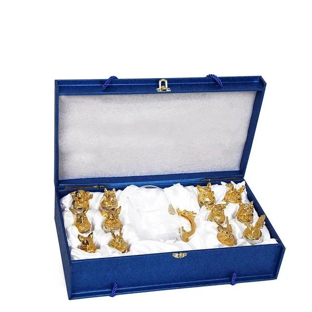 Coffret cadeau bleu ouvert révélant l'ensemble doré : douze verres à shot et leur carafe nichés dans un écrin en satin blanc.