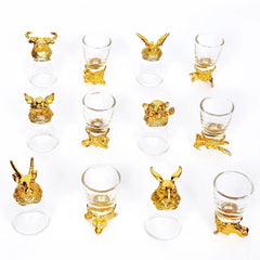Douze verres à shot dorés à motifs animaliers alignés en grille, orientations alternées, sur fond blanc.