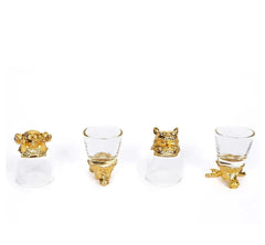 Gros plan sur quatre verres à shot, dont deux ornés de têtes de singe et de tigre dorées.