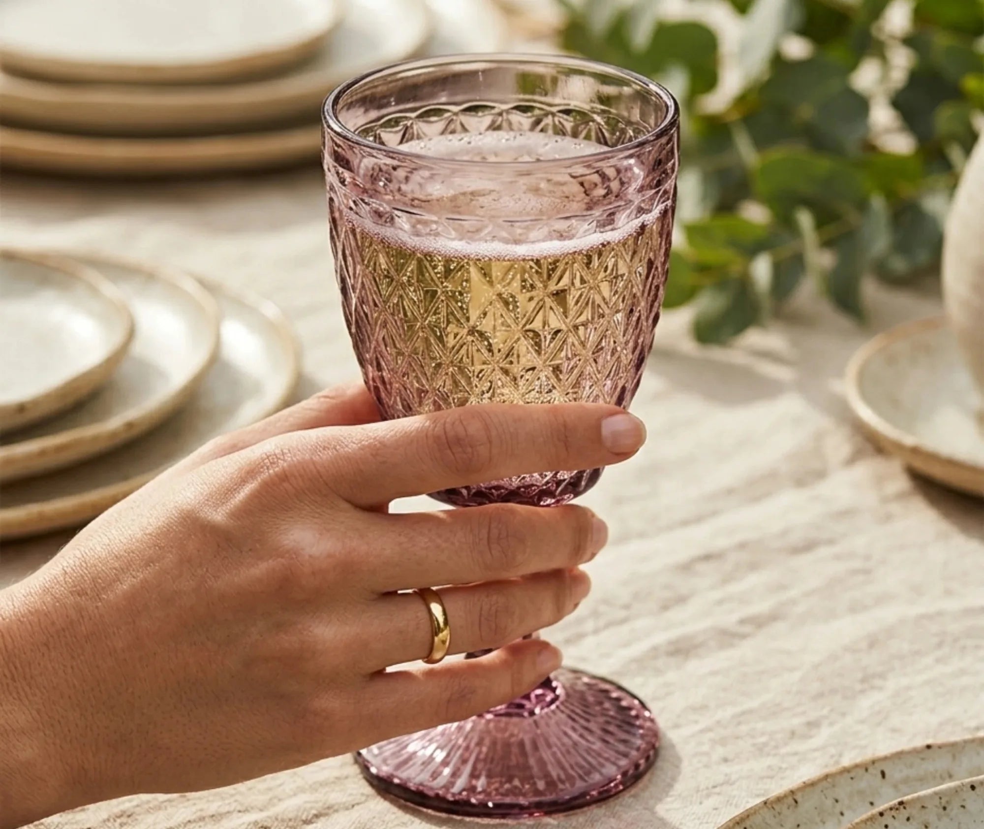 Main tenant un verre à pied rose dragée rempli de champagne sur une table dressée