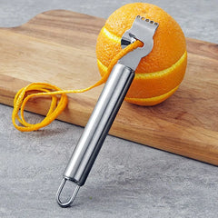 Zeste d'orange en spirale complète posé sur une planche à découper en bois, à côté du zesteur.